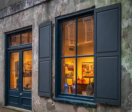 Morning Light on Historic Art Gallery - Charleston, South Carolina Early morning photo of a historic art gallery exterior in Charleston, showing warm light through old glass doors and a window, with a textured stone and concrete facade. Image by Mark Leatherman.