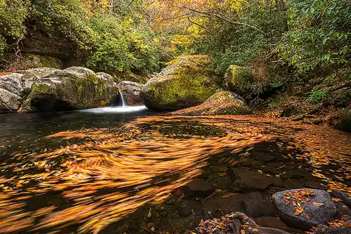 Midnight Hole, Smokies Long exposure photo of swirling autumn leaves in the foreground at Midnight Hole with a small cascade and colorful fall trees in the background. Taken by Mark Leatherman in Great Smoky Mountains National Park.