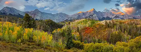 San Juan Mountains at Sunrise Panoramic sunrise photo of the San Juan Mountains near Dallas Divide, with golden aspen and scrub oak in the foreground and rugged peaks lit by morning light. Taken by Scott Ethington.