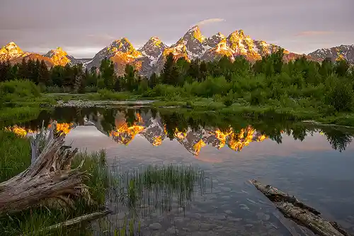 Schwabacher Landing Sunrise Snow-capped Grand Teton mountains at sunrise, warmly lit and reflected in calm water at Schwabacher Landing. Image by Dale Sullivan.