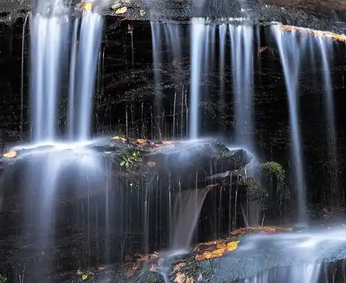 Tom Branch Falls, Smokies Long exposure photo of silky water cascading over rock ledges at Tom Branch Falls, with a few autumn leaves resting on the falls. Taken by Rick Thompson in Great Smoky Mountains National Park.