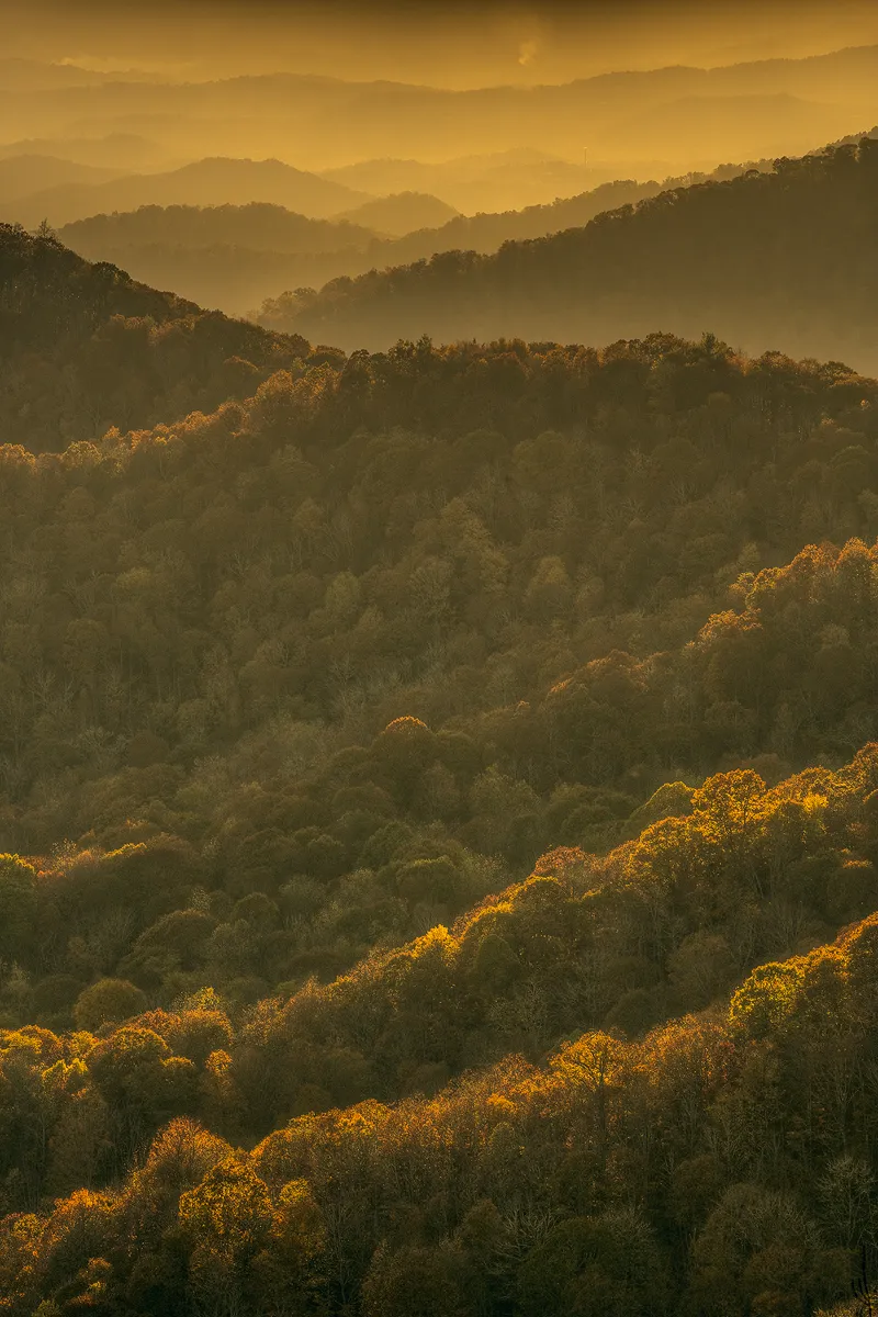 This vertical image was taken from an overlook near Great Smoky Mountains National Park and has a very warm hue to it. A long lens was used, facing west, on a hazy day, in the late afternoon. It shows row after row of ridges. Nearby ones are spread apart a bit more in the bottom of the frame, but they become more tightly packed further back in the distance, in the upper part of the frame where the haze is very pronounced.
