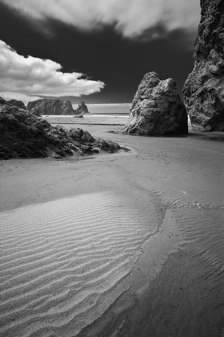 Vertical, black and white image of sand ripples, rocks and sky at Bandon Beach on the Oregon Coast.