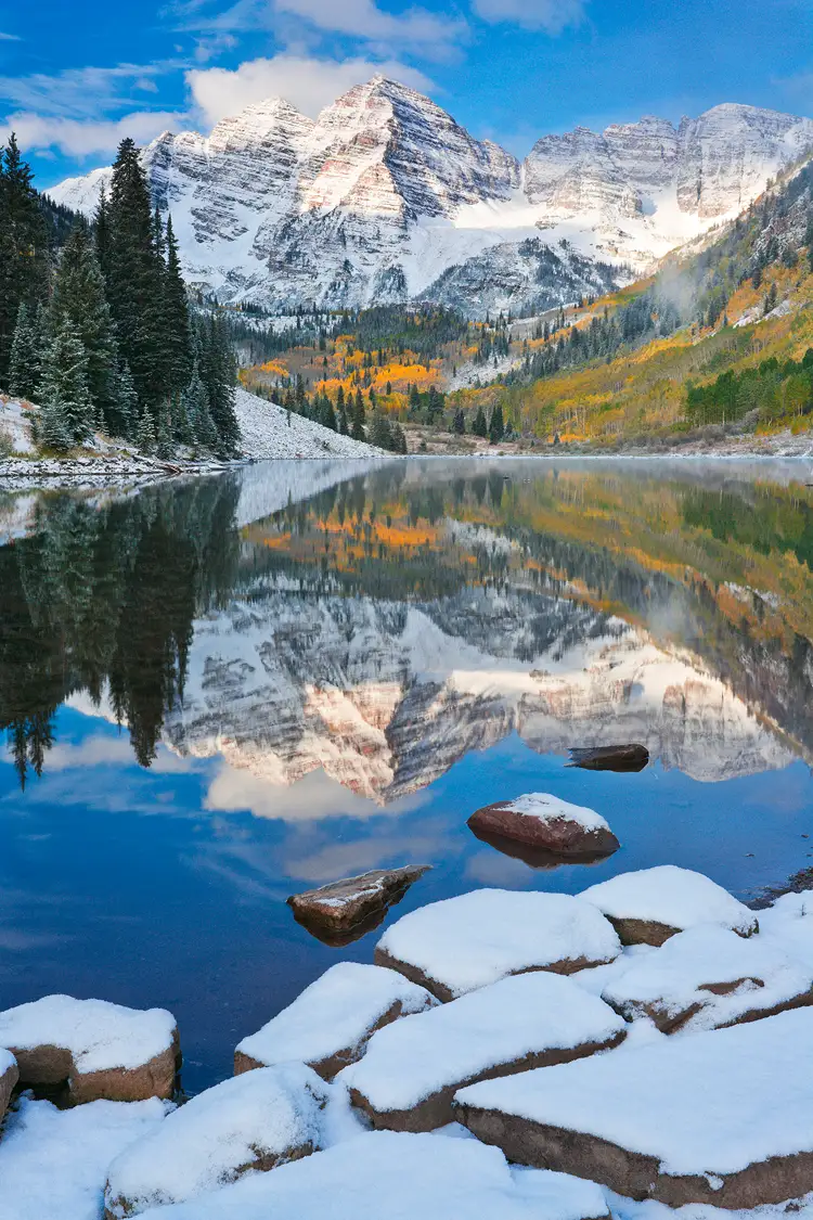 Vertical image of Maroon Bells reflecting in Maroon Lake with a light, autumn snow dusting the scene.