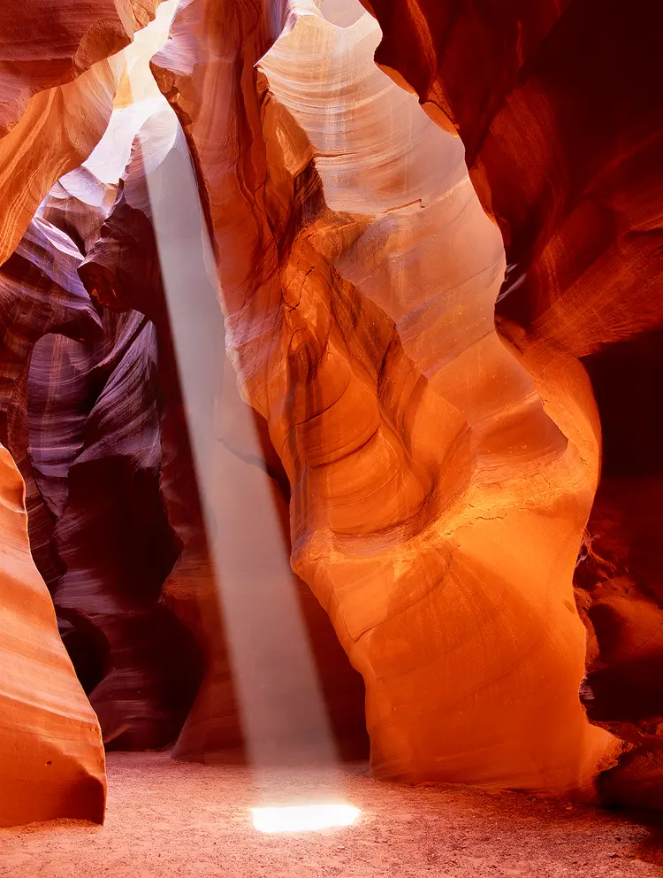 A light beam shines down into the sculpted rocks of Upper Antelope Slot Canyon making it glow orange, as if on fire.