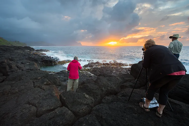 Three photographers photographing sunset on a black rock shore in Kauai.