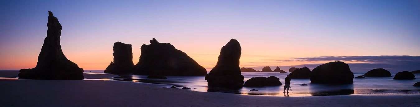 Panorama of a photographer on a rocky beach in purple twilight after sunset.