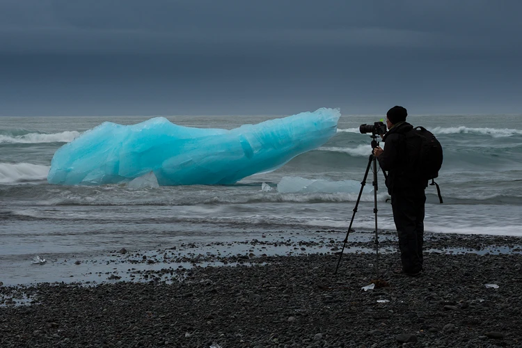 Find Your Inspiration: Read Our Workshop Testimonials A photographer photographing glacial ice on a black beach.
