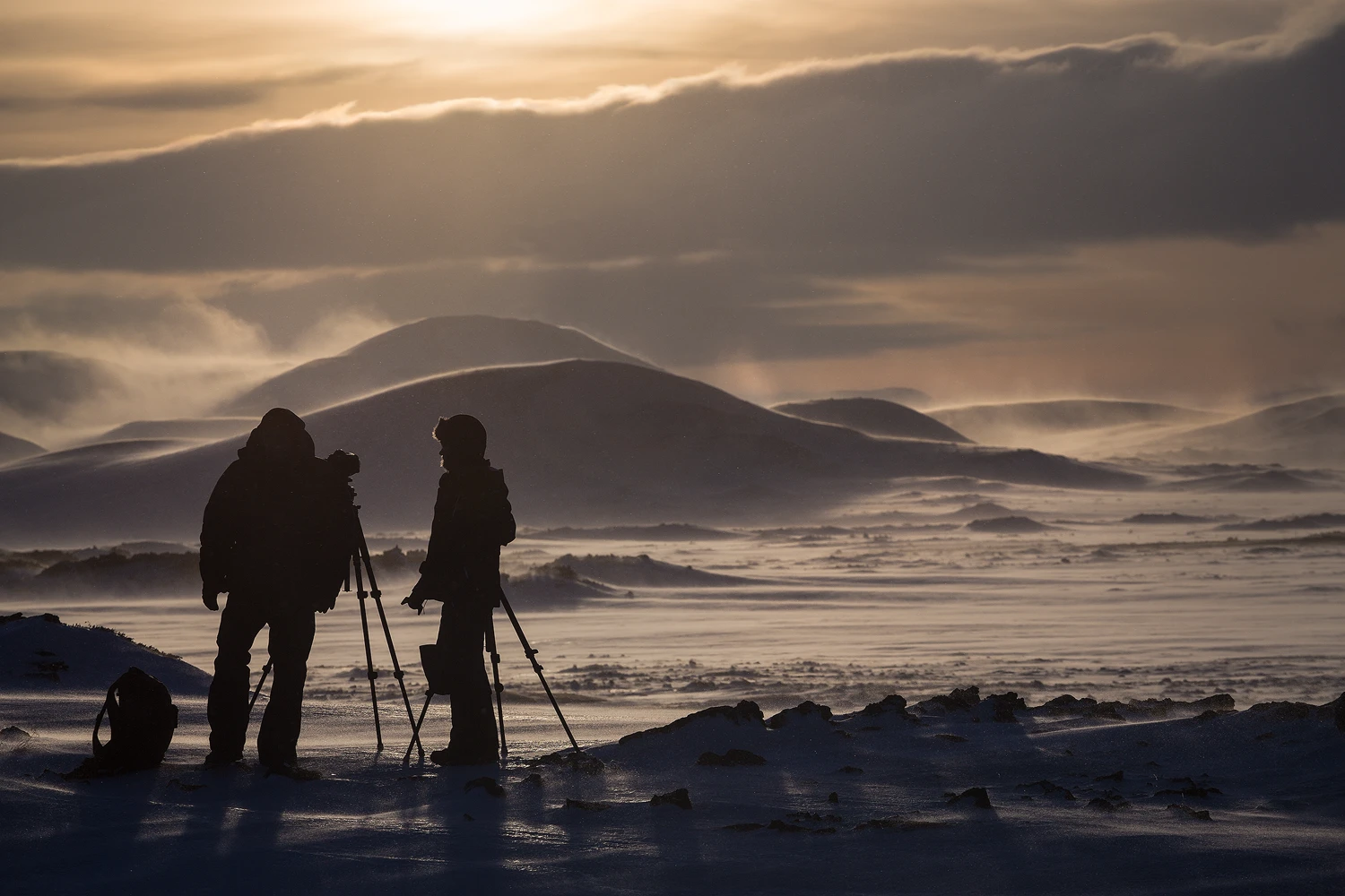 Photographers capturing a winter landscape with blowing snow.