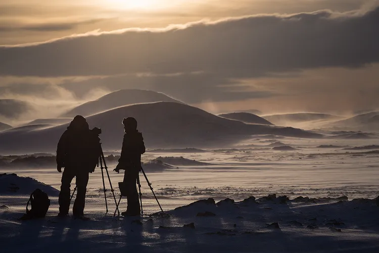 Two photographers standing is a blustery, snowy, winter landscape. 