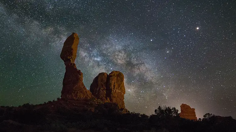 Workshop location; Balanced Rock in Arches National Park sits high in the starry night sky. The Milky Way fills the area behind and around Balanced Rock and diagonals toward the upper, left corner of the image.