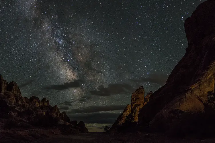 Workshop location; The very bottom of this night image shows a road passing over a small hill. On each side of the road, arid, rocky topography rises dramatically creating a v-shape in the image. The Milky Way fills this v-shape and rises into the sky above the road located near Moab, Utah.