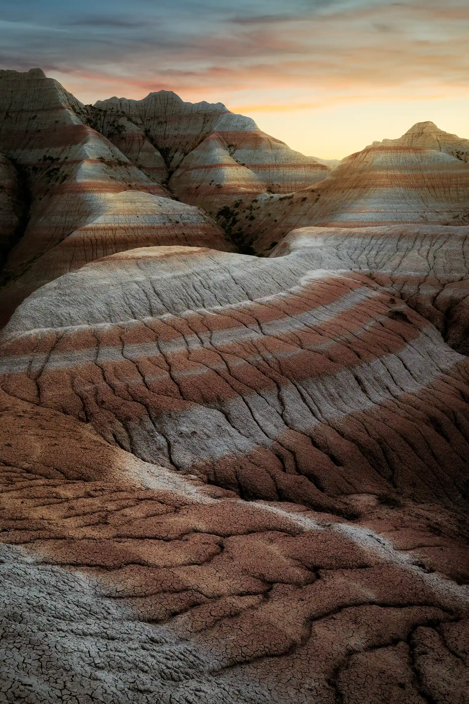Sunset over ridges and layered red and white rock formations in Badlands National Park.