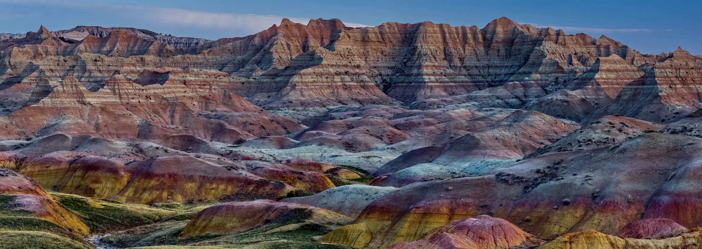 Predawn light on yellow mounds and layered red and white rock formations with distant mountains in Badlands National Park.