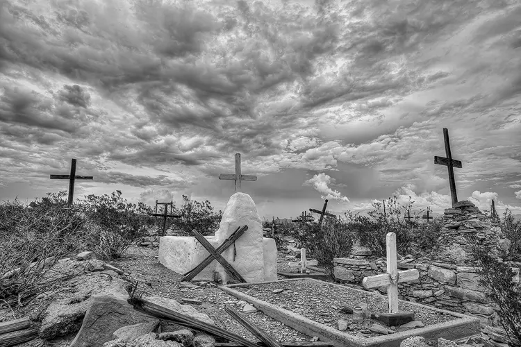 Workshop location; In this black and white image a moody, cloud filled sky broods over the Terlingua cemetery. The neglected desert cemetery, overgrown with bushes, odd piles of rubble and leaning crosses is the perfect match for this tumultuous sky.