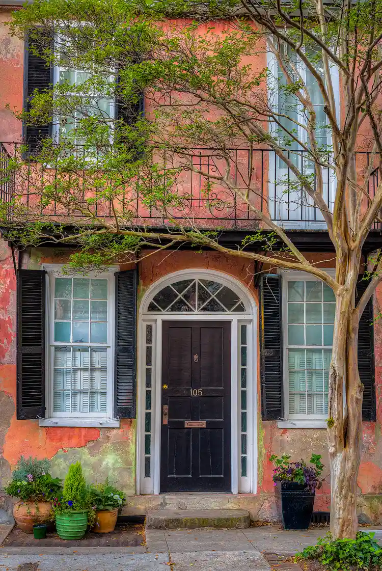 Photography location, Charleston SC; Historic district home with a fading, orange, stucco exterior that contrast nicely with the green, spring foliage in the pots and trees around the home.