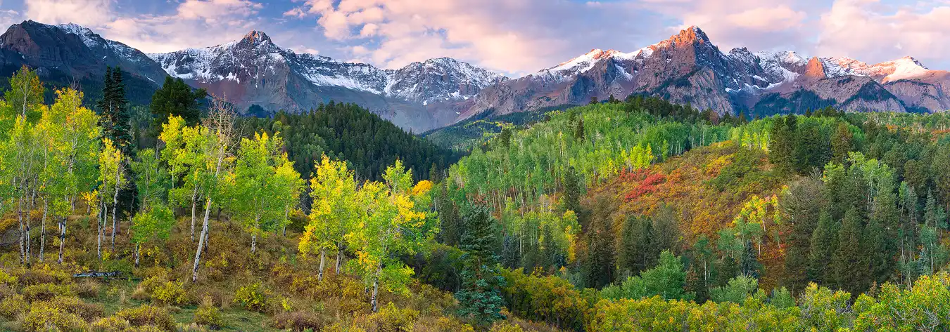 Workshop location; Autumn foliage is beginning to turn on the undulating, foreground hills. Above and behind, snow capped peaks sparkle with the day's first light. The clouds, glowing warmly with sunlight, contrast nicely with the blue sky.