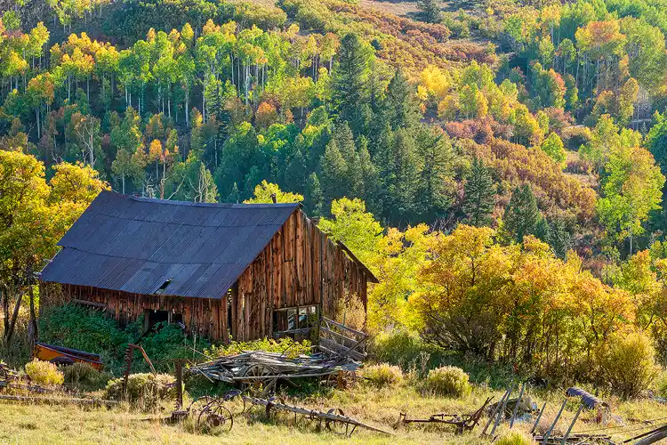 Workshop location; The foreground of this image shows an old, tattered barn surrounded by antique farm implements. Behind is a hillside ablaze with Colorado autumn colors.