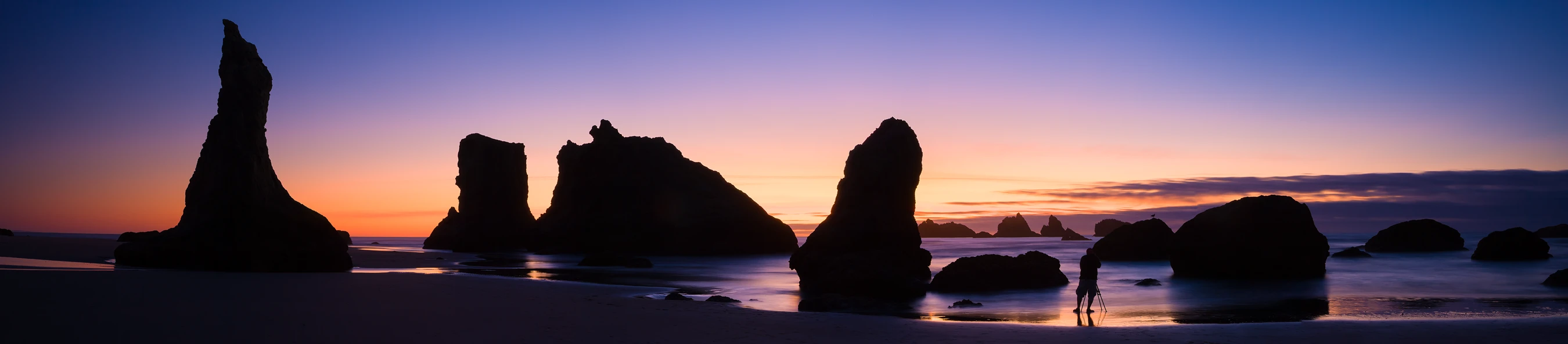 Twilight at Bandon Beach with sea stacks and reflections on wet sand.