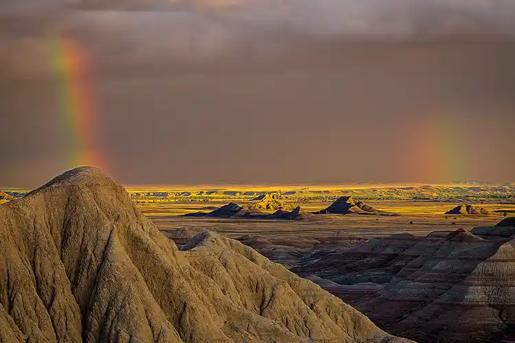 Rainbow beside a rugged ridge above the Badlands in the last light of evening at Badlands National Park.