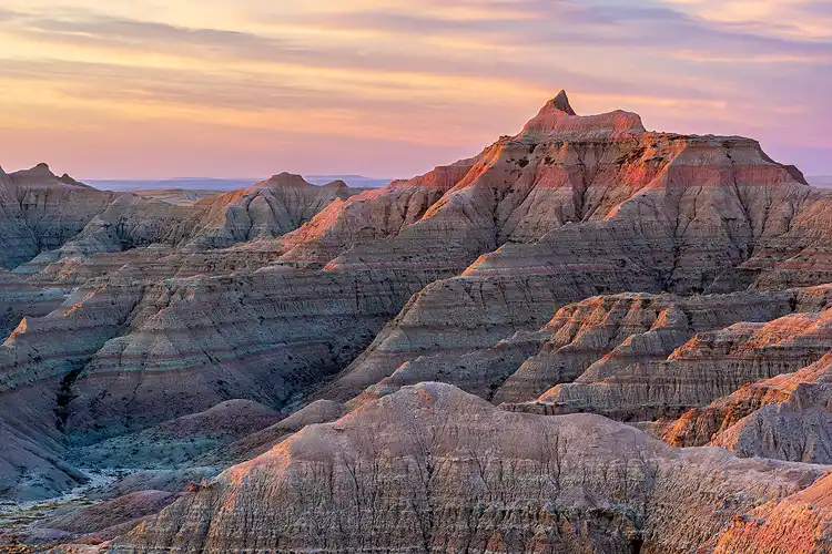 First light of sunrise tracing across layered ridges and buttes in Badlands National Park.