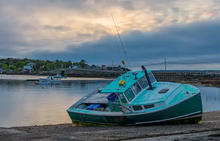Fishing boat resting on the harbor bottom at low tide beneath soft evening clouds in Port Clyde, Maine.