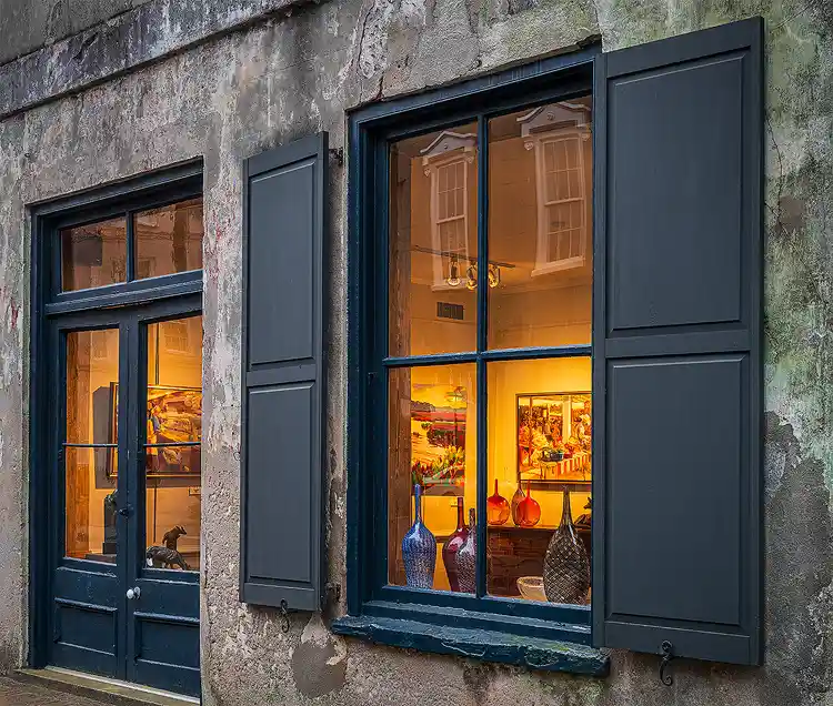 Warm light illuminating artwork through the window of a weathered Charleston gallery.