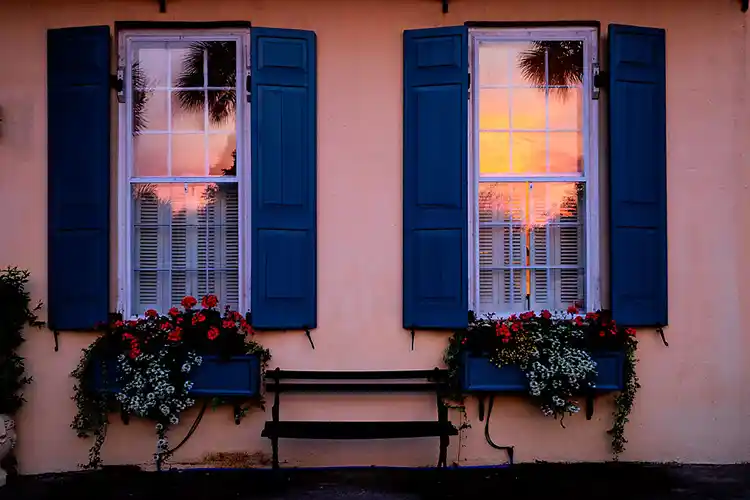 Morning sky reflected in the windows of a Charleston home with blue shutters.