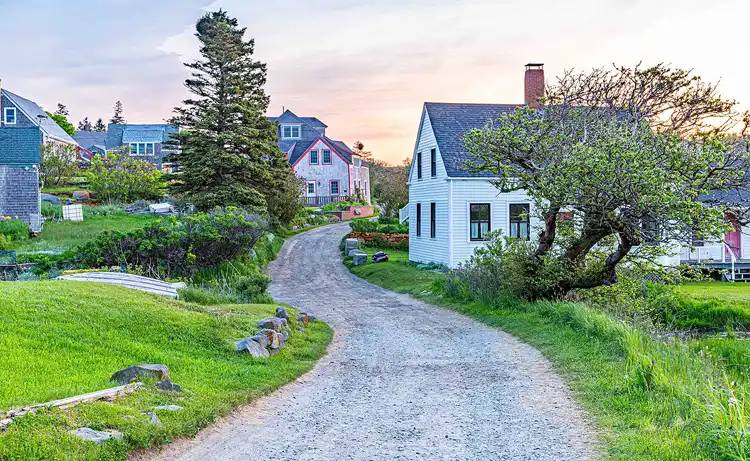 A narrow gravel lane winds between weathered cottages beneath the soft morning light on Monhegan Island, Maine.