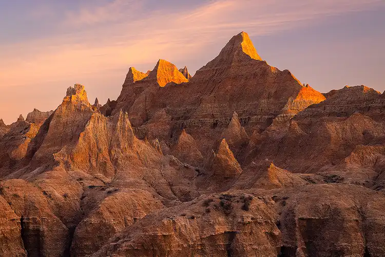 First light of sunrise illuminating the highest pinnacles at Norbeck Pass in Badlands National Park.