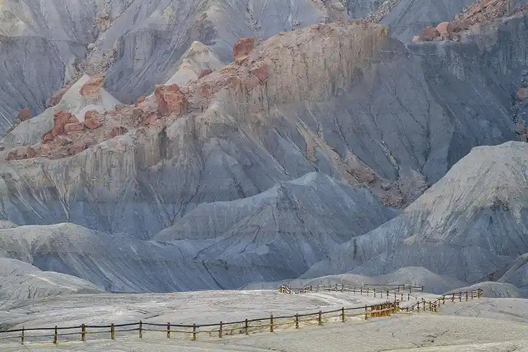 Weathered fence winding across pale Bentonite Hills toward the colorful cliffs of North Caineville Mesa near Hanksville, Utah.