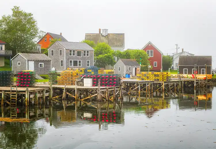 Weathered waterfront buildings and colorful lobster traps along Port Clyde Harbor, Maine.
