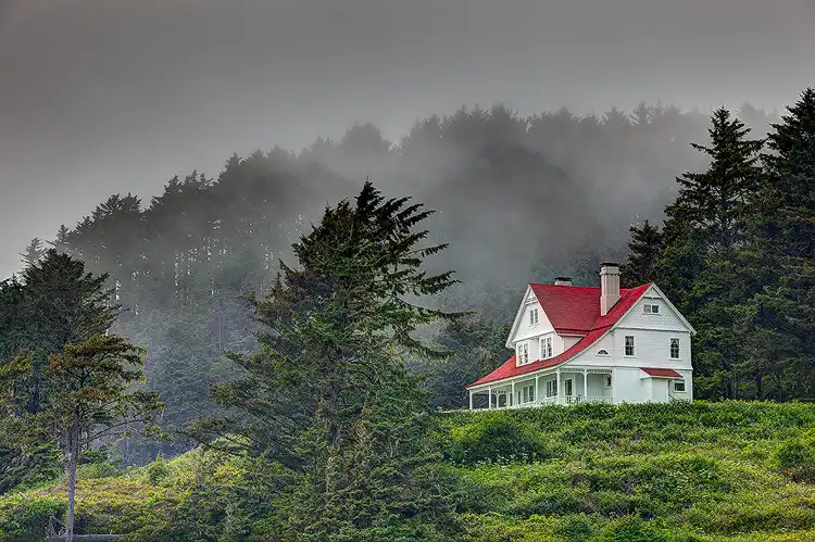 Heceta Head Lighthouse Keeper's House overlooking the Oregon coast with fog drifting through the surrounding forest.