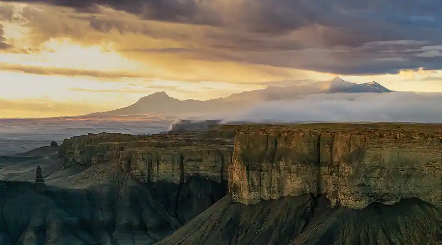 Morning light illuminating towering cliffs as fog drifts across the Henry Mountains from Moonscape Overlook near Hanksville, Utah.