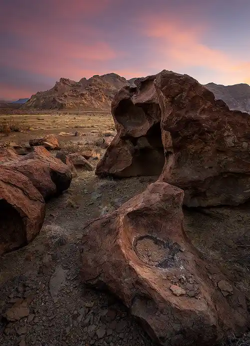 Weathered volcanic boulders with sculpted cavities at Indian Head beneath a colorful sunset in Big Bend National Park.