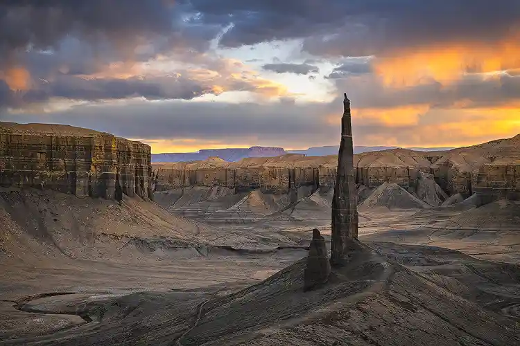 Long Dong Silver rising above the gray badlands beneath glowing sunset clouds near Hanksville, Utah.