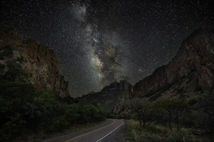 Chisos Basin Road leading toward the Milky Way between towering canyon walls in Big Bend National Park.