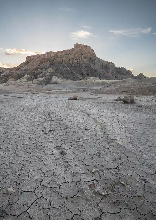 Cracked clay badlands leading to North Caineville Mesa beneath soft evening light near Hanksville, Utah.