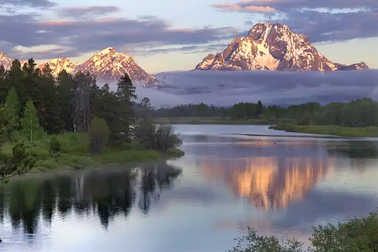 Mount Moran reflected in the Snake River at Oxbow Bend beneath a band of morning fog at sunrise, Grand Teton National Park.