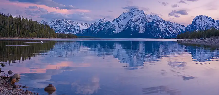 Mount Moran reflected in the calm waters of Jackson Lake beneath a colorful sunset sky, Grand Teton National Park.