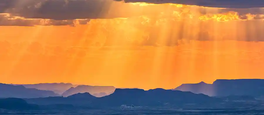 Sunbeams breaking through storm clouds above layered desert mountains from Sotol Vista in Big Bend National Park.