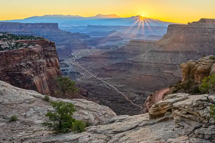Sunstar rising above the canyons as the White Rim Road winds through Canyonlands National Park.