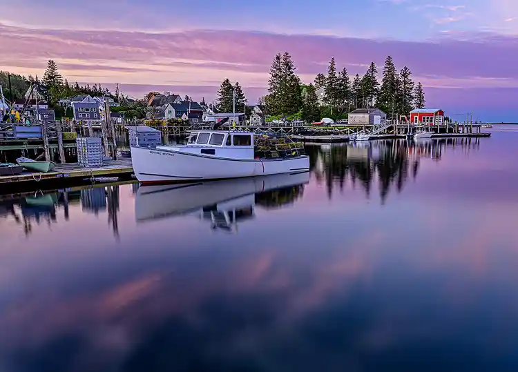 Lobster boat reflected in the calm harbor at sunrise in Port Clyde, Maine.