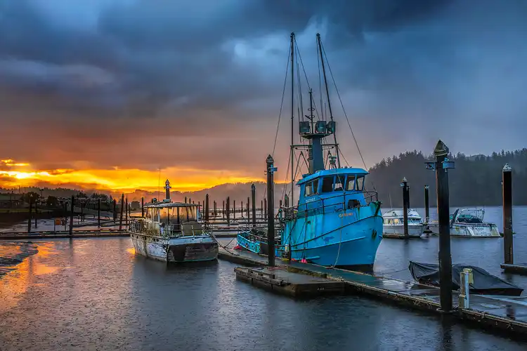 Commercial fishing boats in Florence Harbor beneath a stormy sunrise on the Oregon coast.