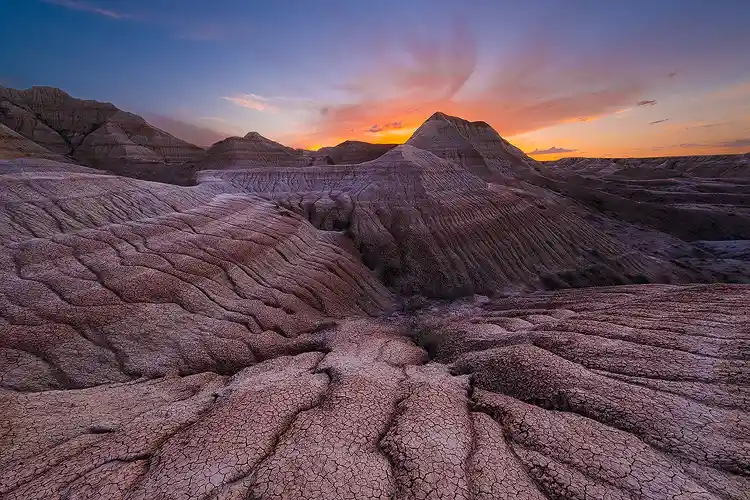 Branching erosion patterns leading toward a layered butte silhouetted against the last glow of sunset in Badlands National Park.