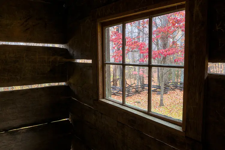 Workshop location; The image is from inside a historic cabin in Great Smoky Mountains National Park. A window, the subject, and some of the cabin interior wall is shown. Viewing through the six panes of the window, three on top, three on bottom, one sees an old zig zag fence and a dogwood tree with red, autumn leaves.