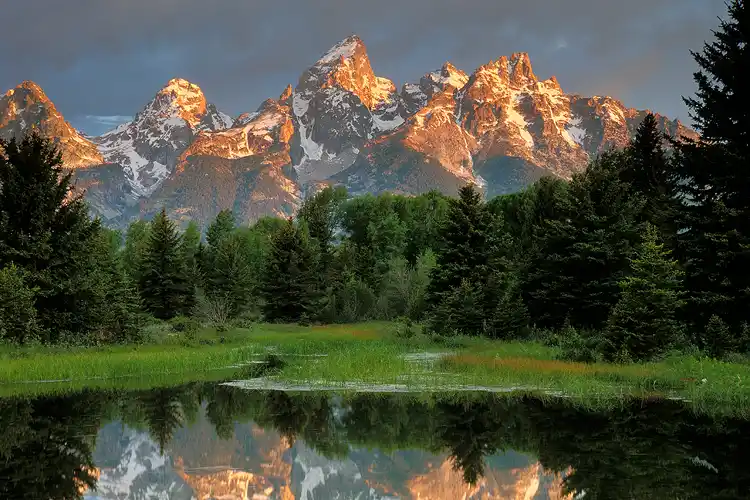 Workshop location; Puffy gray clouds catch just a hint of the warm, morning light that drenches the snow capped mountain peaks which reflect in a calm pool of the Snake River at Schwabacher Landing in Grand Teton National Park, near Jackson, WY.
