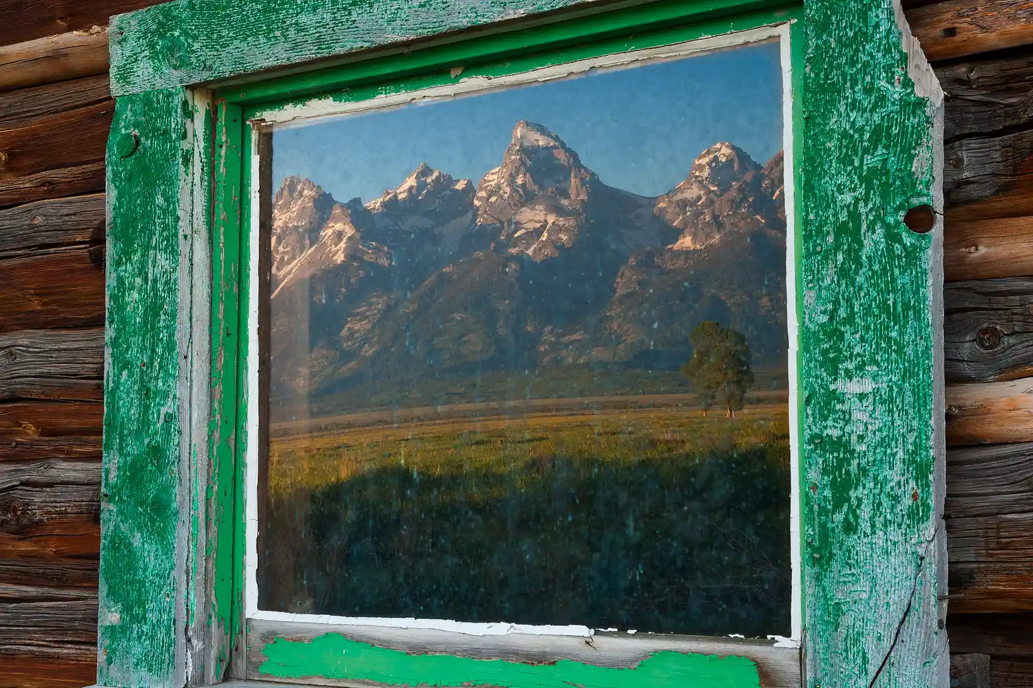 The Grand Teton range reflected in a cabin window.